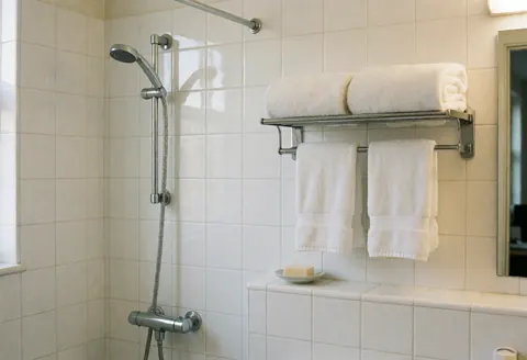 Clean bathroom with white tiles, chrome shower, white towels on rack, and soap dish for lodging