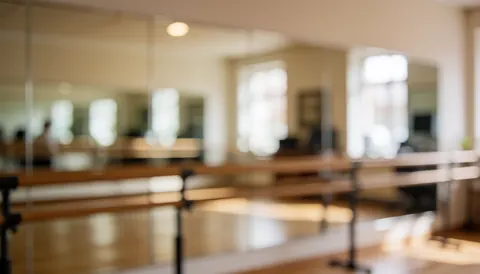 Soft focus background of a dance studio featuring wooden barres, mirrors, beige walls, and warm lighting, ideal for text overlay.