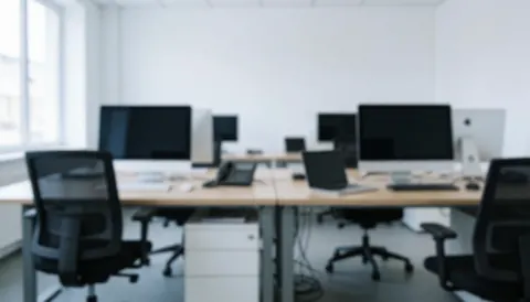 Clean modern office space featuring white desks, chairs, and computer monitors, providing a professional background for text.