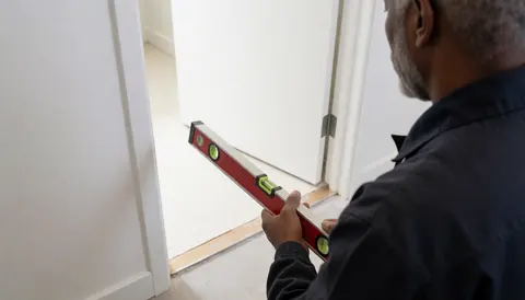 Worker installing bathroom threshold with a level, white walls and clean floor for bathroom installer website