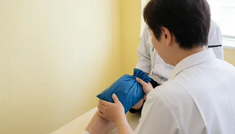 Therapist applying cold treatment to a client's knee using a blue sleeve against a yellow wall with copy space