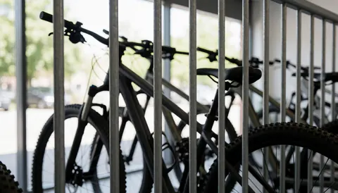 Industrial background featuring mountain bikes parked behind a metal fence, suitable for a mountain bike coaching business text overlay.