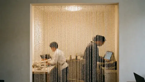 Pearl bead curtain separating a modern workspace with desks, laptops, white walls, and professional ambiance.