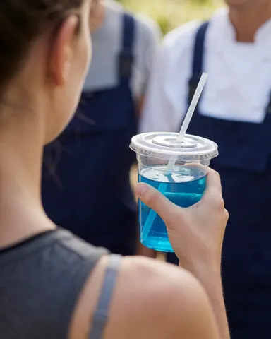 A person holding a plastic cup with a blue beverage at an outdoor adventure park with staff in work clothes in the background