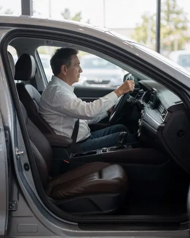 A customer testing a sedan with leather seats, viewed from the exterior at a car dealership.