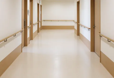 Wide accessible hallway featuring wooden handrails, smooth flooring, and clean white walls suitable for a geriatric massage center.