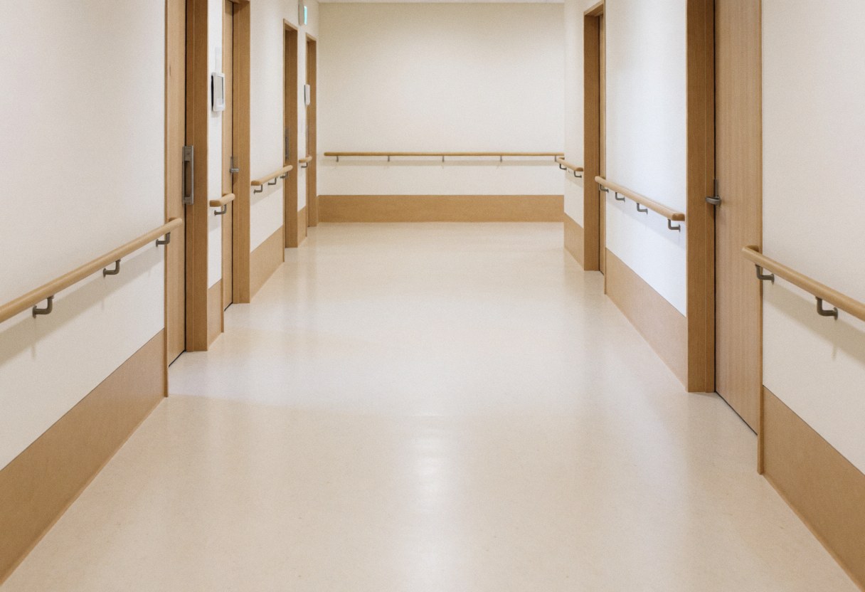 Wide accessible hallway featuring wooden handrails, smooth flooring, and clean white walls suitable for a geriatric massage center.