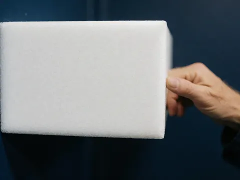 Hand holding a white EVA foam block against a dark blue wall, highlighting clean texture for fitness training