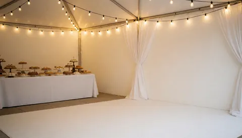 White tent decorated with string lights and a candy table in the background, ideal for party coordinators