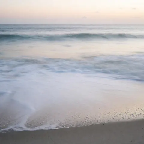 Long exposure shot of Copacabana beach showing misty waves, dark sand, and a soft sunset sky