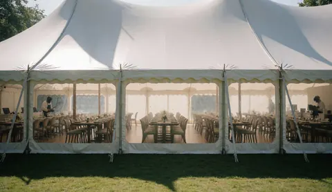 White banquet tent with tables and chairs arranged, staff working inside, natural light, outdoor garden