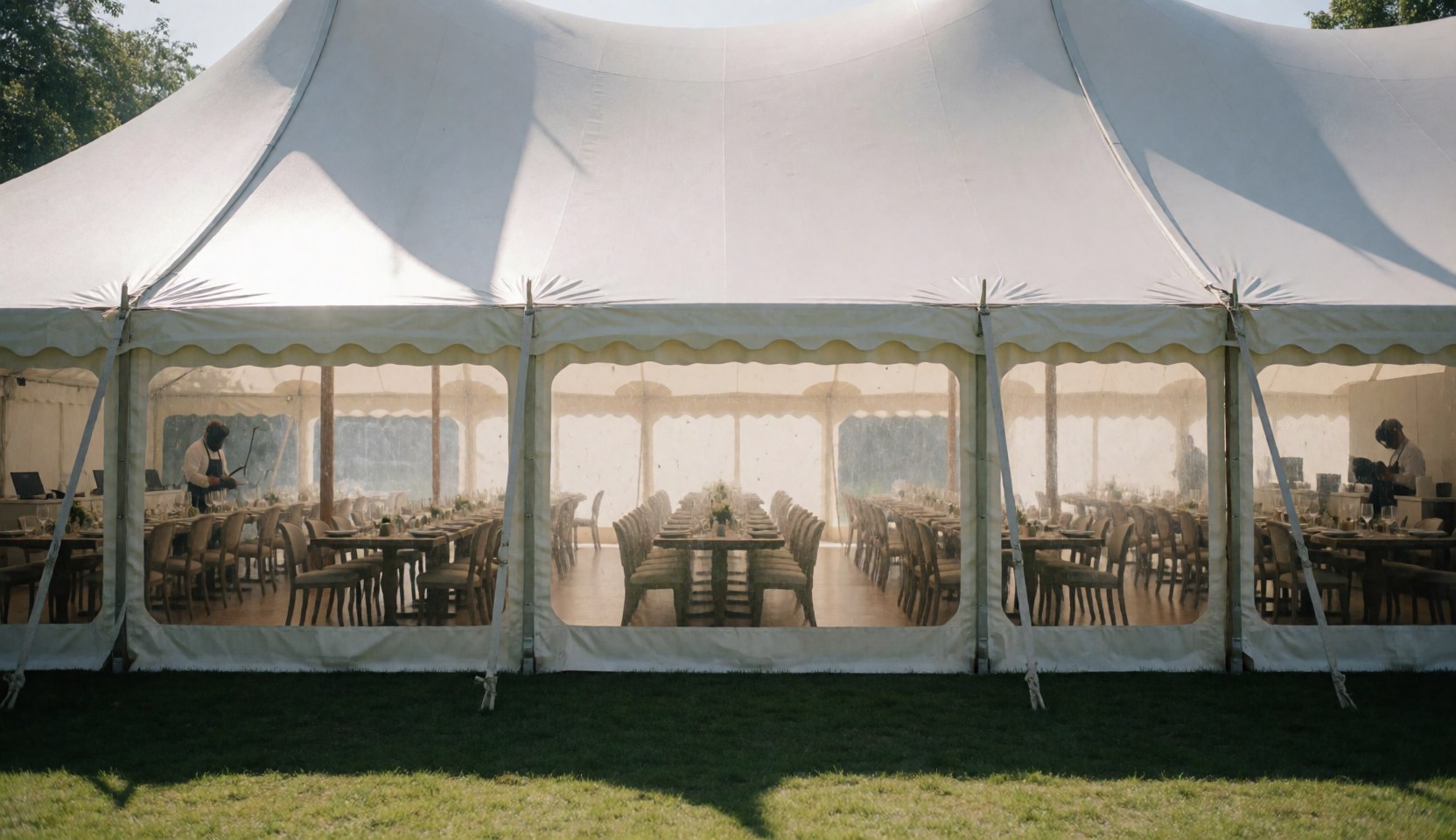 White banquet tent with tables and chairs arranged, staff working inside, natural light, outdoor garden