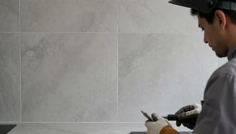 Kitchen installer working on a gray porcelain wall with a tool in hand, professional and clean scene