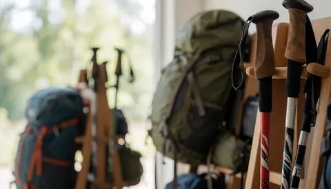 Hiking poles and mountain backpacks on wooden racks with a blurred natural light background, ideal for mountain refuge text overlay.