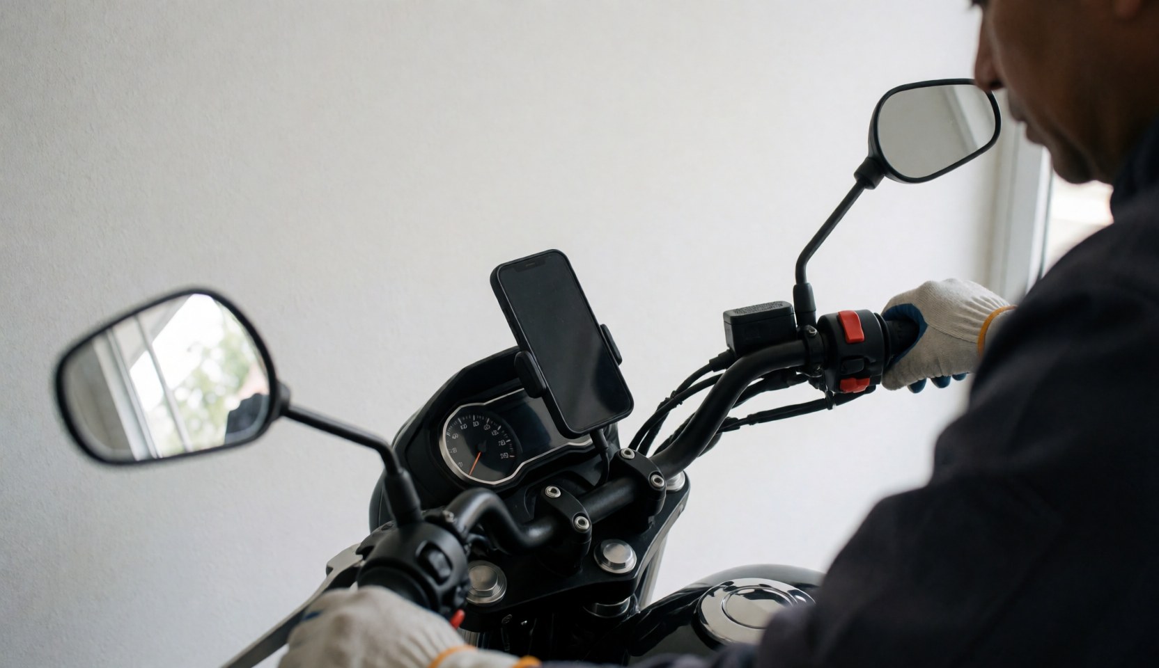 Close-up of a motorcycle taxi handlebar with a smartphone secured in a holder, showing a gloved hand and white wall background