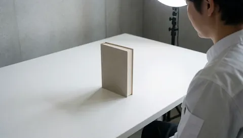 Professional product photographer in a studio with a hardcover book on a white table and concrete wall, lit by studio light.