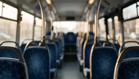Interior view of a public bus featuring blue seats and metal railings illuminated by warm sunset light, suitable as a background for text.