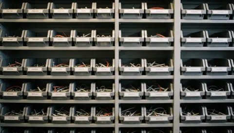 Shelves holding organized boxes of electronic components and screws for console repair, providing a professional neutral background for text.