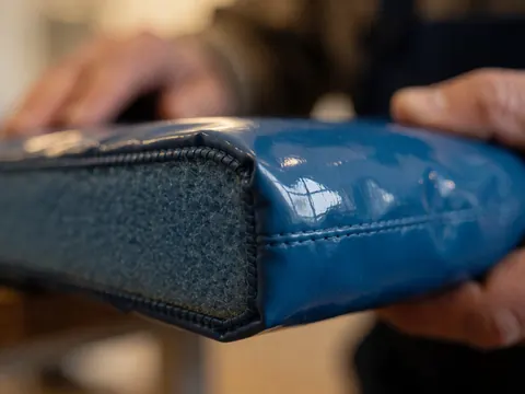 Close-up of the corner of a blue gymnastics mat showing visible stitching, window reflection, and exposed foam texture.