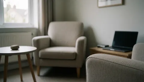 A therapy room featuring comfortable chairs, a small side table with a stone, and natural light, suitable for hypnotherapy text backgrounds.