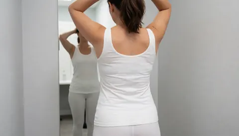 Back view of a woman adjusting her hair in front of a mirror in a dressing room with light gray walls