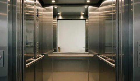 Interior of a modern elevator featuring stainless steel walls, metal handrails, and a control panel, suitable for elevator repair services.