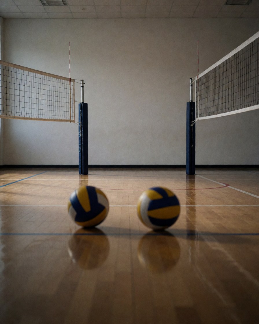 Two yellow and blue volleyballs resting on the wooden floor of an empty indoor court, perfect for sports training promotion