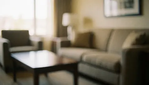 Apartment hotel living room background featuring a sofa and coffee table with natural light and neutral walls, ideal for advertising text overlay.