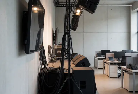 Empty event stage featuring professional speakers, cables, and lighting against concrete walls, ready for a presentation.