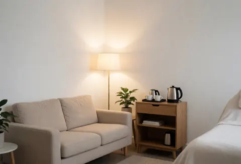 Modern waiting room featuring a beige sofa, lamp, side table with coffee, and plants for a cozy beauty salon atmosphere.