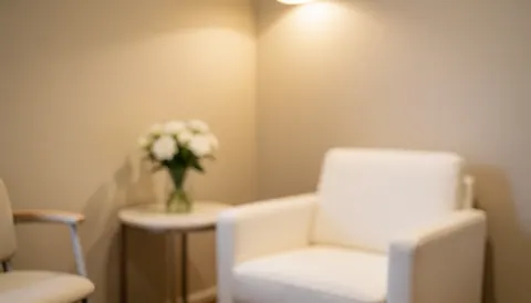 White chairs arranged in a beige waiting room with a small table holding white flowers, ideal for beauty salons or spas.
