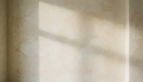 Soft cream textured wall with diffused light and window shadow, ideal background for text in cafes or decorative spaces.