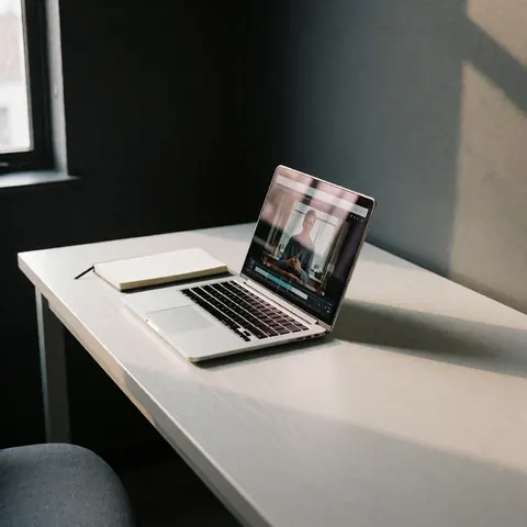 Open laptop showing a programming course, next to a notebook, on a white desk in an office with gray walls and natural light