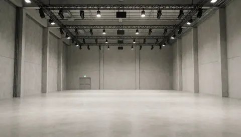 Empty event space with concrete walls, metal ceiling structures, and professional lighting, ideal for presentations.