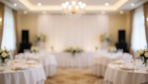 Background of a wedding reception featuring round tables with white tablecloths, floral arrangements, and warm lighting, suitable for event audio services.