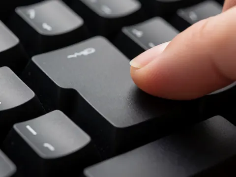Close-up detail of a finger pressing a black mechanical keyboard key, highlighting texture and studio lighting on the plastic surface.