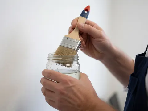 Close-up of a hand holding a paintbrush in a jar of solvent for cleaning, white background