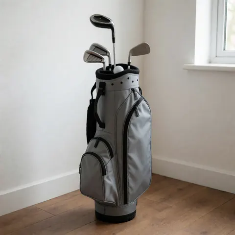 Gray golf bag containing clubs and a ball placed on a wooden floor against a white wall, suitable for golf instructor business use