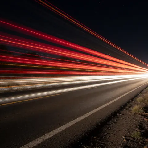 Long exposure photo showing red and white light trails from moving vehicles on a dark road, suitable for artistic photography business backgrounds.