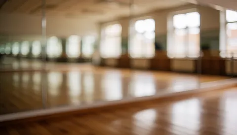 Empty gymnastics studio background featuring large mirrors, wooden flooring, and windows, suitable for text overlays about gymnastics classes.