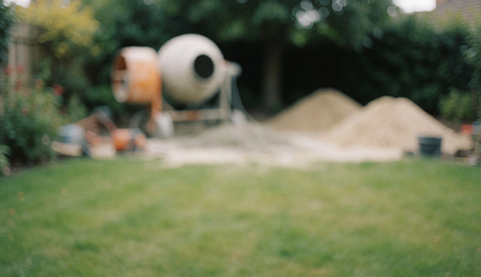 Blurred garden background featuring a concrete mixer and piles of sand, suitable for pool installation text overlays