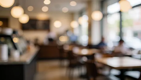 Soft focus background of a coffee shop interior featuring tables, chairs, and hanging lights, suitable for text or logo placement.