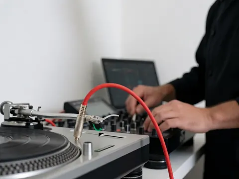 Close-up of a red audio cable plugged into a vinyl turntable and mixer on a white table.