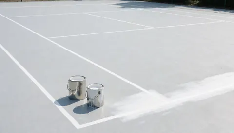 Two white paint cans resting on a tennis court with freshly painted white lines, suitable for tennis court installation services