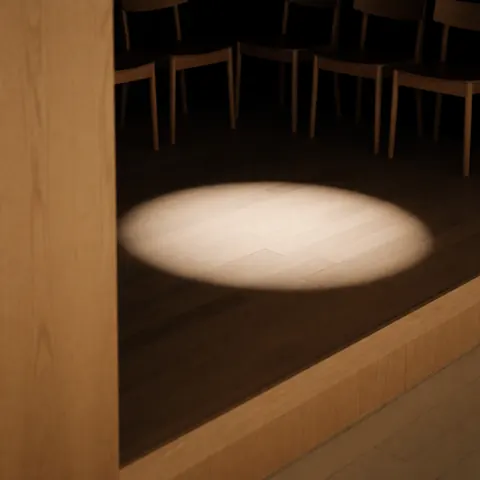 Empty wooden stage with focused warm light on the floor and wooden chairs in the background, ideal for oral presentations