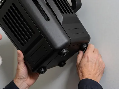 Close-up of hands adjusting a black professional stage spotlight with ventilation slots against a gray wall for event lighting setup