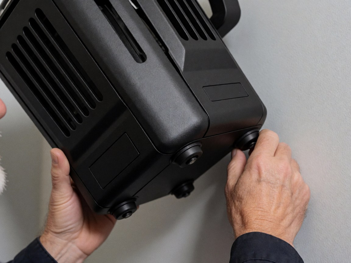 Close-up of hands adjusting a black professional stage spotlight with ventilation slots against a gray wall for event lighting setup