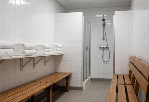 Clean shower room featuring wooden benches, stacked white towels, and a glass shower enclosure, suitable for a yoga center.