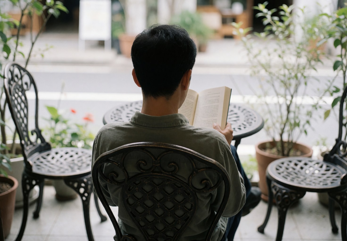 A man reads a book while seated in a wrought iron chair on a plant-filled terrace, suitable for a bed and breakfast setting.