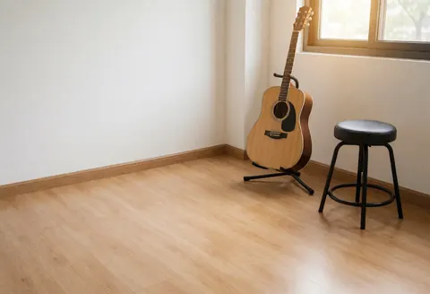 Acoustic guitar on a stand next to a chair in a music studio with wooden floors and white walls, suitable for music classes.